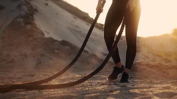 Sporty Woman Training Around the Sand Hills at Sunset Hits the Rope on the Ground and Raised the