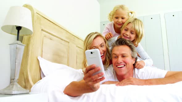 Happy family taking a selfie on mobile phone in the bed room 4k