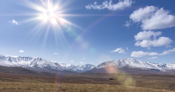 Timelapse of Sun Movement on Crystal Clear Sky with Clouds Over Snow Mountain Top. Yellow Grass at