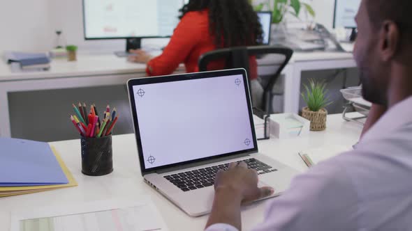 Happy african american businessman sitting at desk, using laptop with copy space in modern office