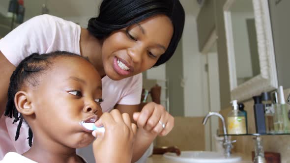 Mother teaching her daughter to brush her teeth in bathroom
