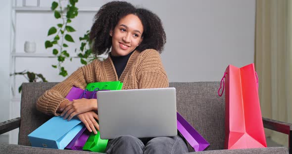 Afro American Woman Girl Teenager with Laptop Sits on Couch Sofa in Interior of Living Room Hugs