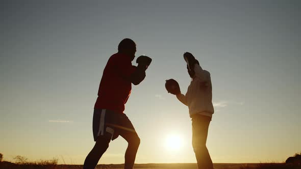 Black Man Trains to Boxing with Trainer Outdoors Against Background of Sunset Bottom View