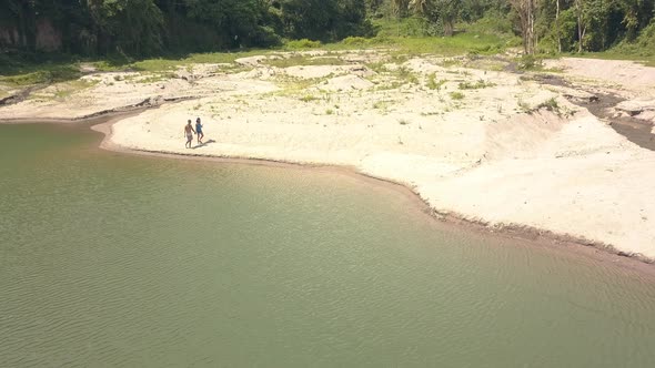 Couple Man and Woman Are Walking on the Sand Beach on Lake Among Tropical Forest, Aerial View.
