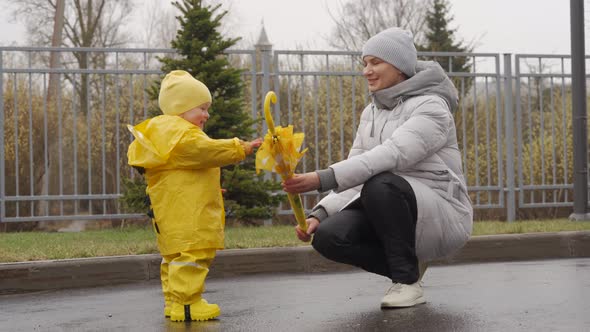 Mother with Small Cute Child in Yellow Waterproof Rain Pants Raincoat and Rubber Boots for Kids