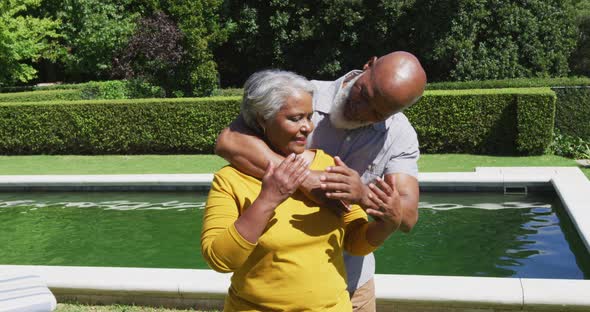 Senior african american couple in love smiling and embracing by swimming pool in sunny garden