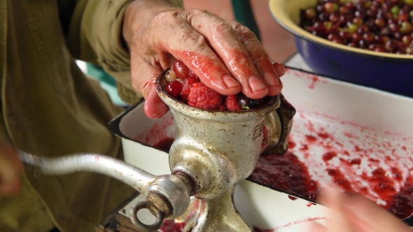 Human's hands chops summer berries for jam in grinder closeup