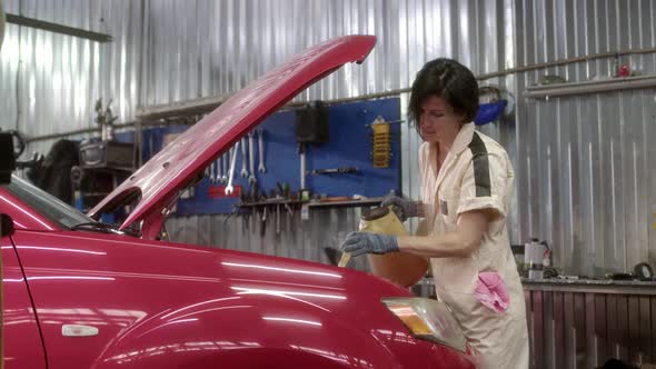 Woman Mechanic in Light Beige Overalls Pours Oil Into Car From Special Watering Can in Car Service