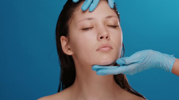 Cosmetic Surgeon Examing Female Head and Face Before Operation on Blue Background