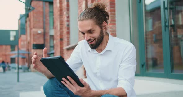 Man Reading Good News on Tablet Device and Joyful Showing Happy Emotions when Sitting in Stairs