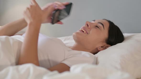 Latin Woman Talking on Smartphone Laying in Bed