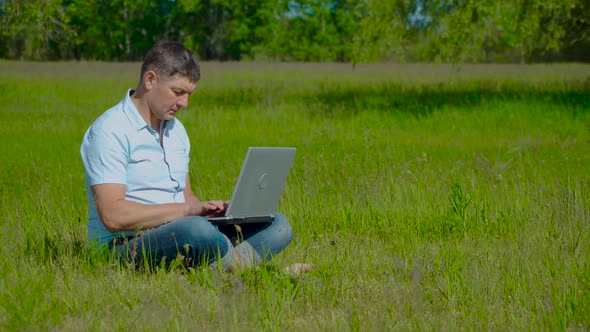 Businessman Works Behind a Laptop Sitting on the Grass