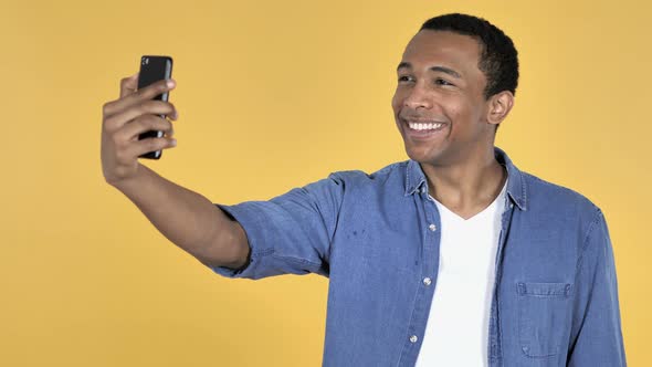 Young African Man Taking Selfie with Smartphone Yellow Background