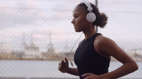 Young Woman In Sportswear And Headphones Jogging Along Harbour