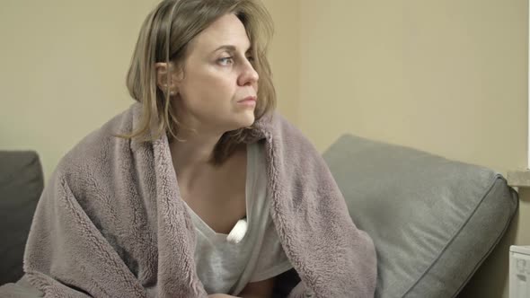 Young Woman Sits Wrapped in a Blanket and Measures the Temperature