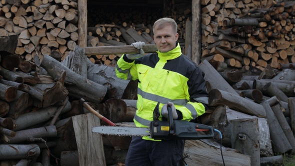 Lumberjack Worker. Man Woodcutter Holds Big Axe and Electric Chainsaw on His Hands. Firewood