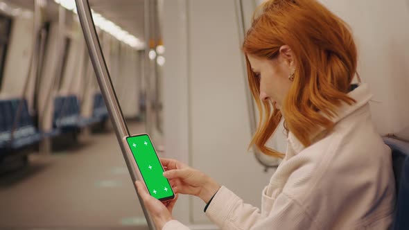 Tourist woman sitting in metro and scrolls the green screen phone on the train.