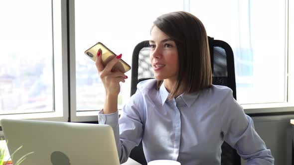 Confident businesswoman holding smartphone near mouth for recording voice message