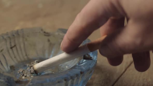 Smoker flicking ash off a burning cigarette into an ashtray