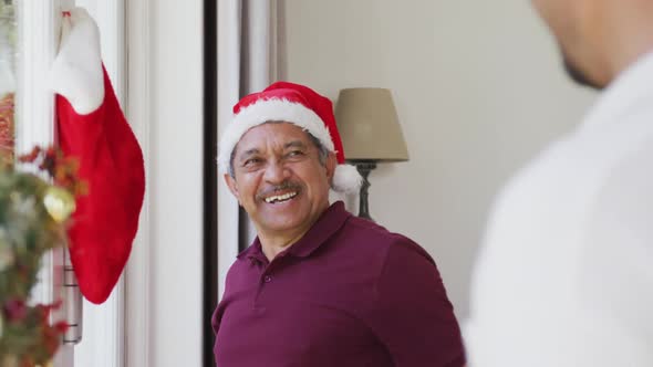 Cheerful senior man hanging christmas sock on window and patting son at home