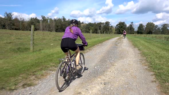 Following behind a woman biking with her son in the distance on a beautiful day with big puffy cloud