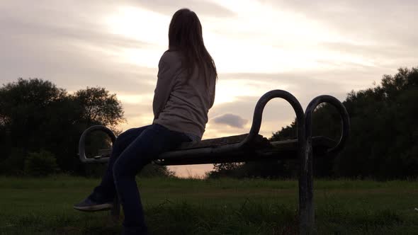 Woman sitting on a park bench at sunset looking at the view