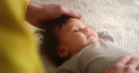 Happy Young Father Strokes Newborn Baby Lying in a Child Crib