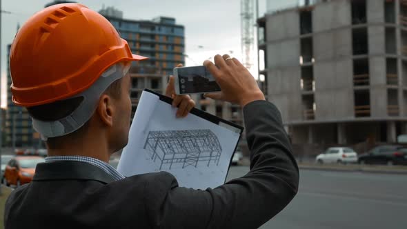 Engineer with the Smart Phone Taking Pictures of Construction