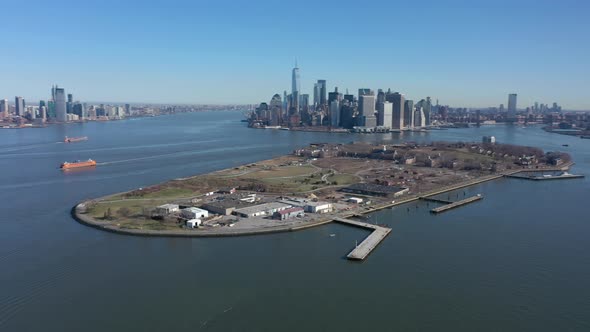 An aerial view over New York harbor on a sunny day with blue skies. The camera truck right and pan l