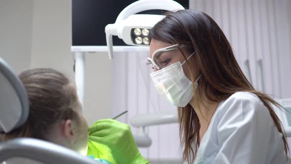 Friendly Female Dentist Examines Teeth of a Cute Little Girl Using Her Instruments