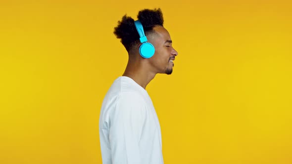 Handsome African Man Having Fun, Dancing with Blue Headphones in Yellow Studio. Side, Profile View