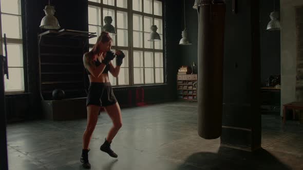 Athletic Fit Female Boxer Exercising Punches with Boxing Bag in Gym During Kickboxing