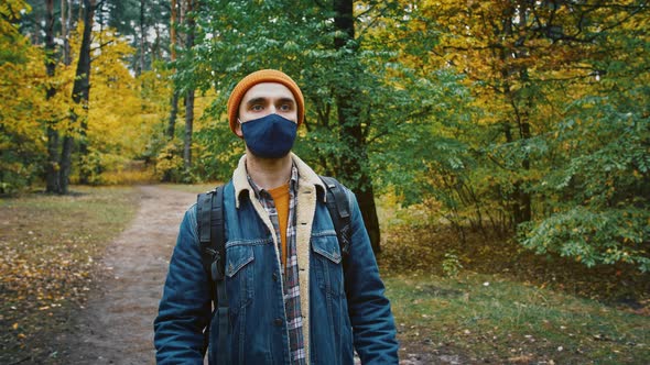 Young Male Backpacker Taking Off Protective Mask and Enjoying Fresh Air Walking in Autumn Forest