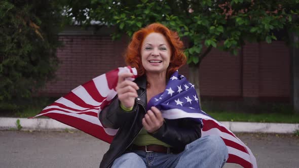 Zoom in Smiling Confident Beautiful Retro Woman Sitting on Skateboard Wrapping in American Flag