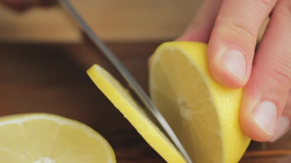 Male hand with big knife slicing lemon citrus fruit on the cutting board at kitchen