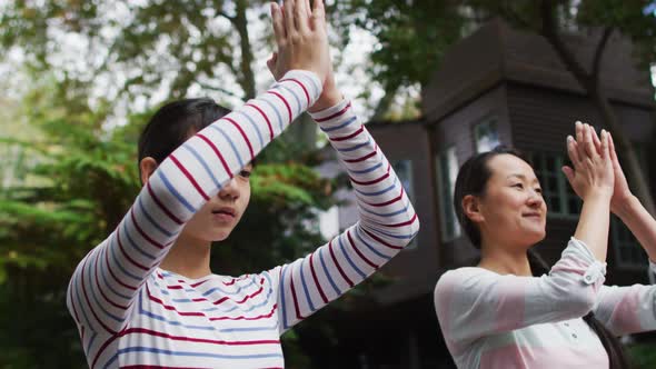 Happy asian mother exercising in garden with daughter, practicing tai chi together