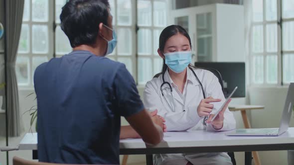 Asian Female Doctor Showing Analysis Results On Tablet Computer To Male Patient During Consultation