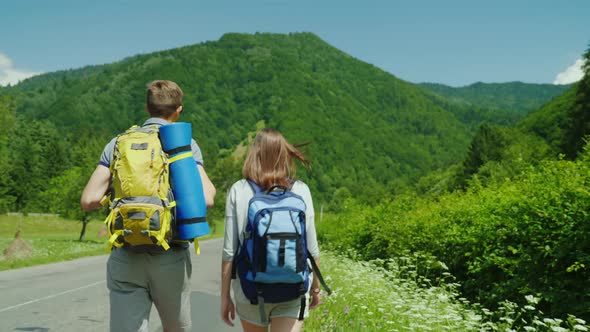 A Young Tourist Couple Walks Along the Road to Beautiful Mountains Covered with Forest