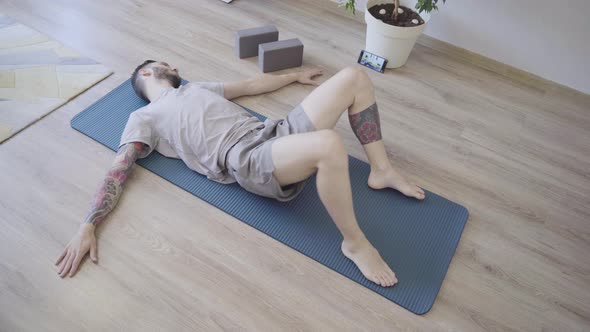 Young Man Relaxing and Doing Reclined Spinal Twist Yoga Pose at Home