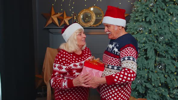 Grandfather Gifting Christmas Present Box to Surprised Grandmother Senior Couple in Santa Claus Hats