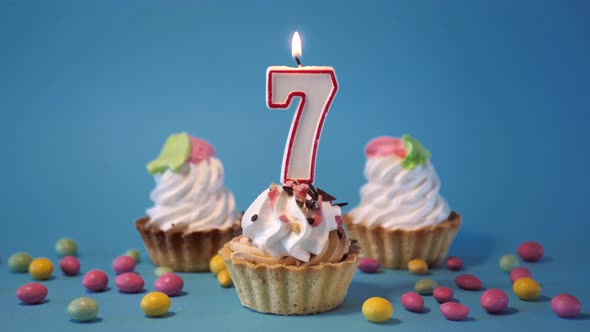 Cake Birthday Cupcake with a Burning Candle Number Seven 7 on a Blue Background