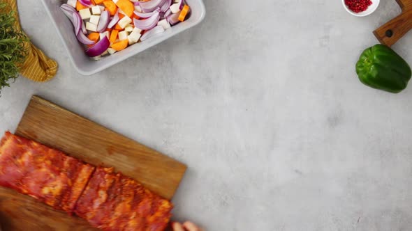 Anonymous person arranging raw ribs and vegetables on table