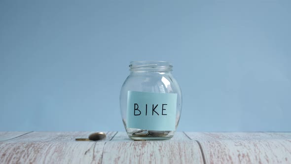 Saving money for bike. Throwing coins into glass jar with inscription bike