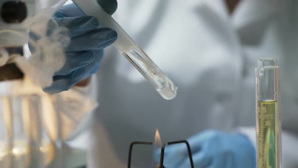 Chemistry Student Holding Tube With Boiling Fuming Liquid Over Burner in Lab