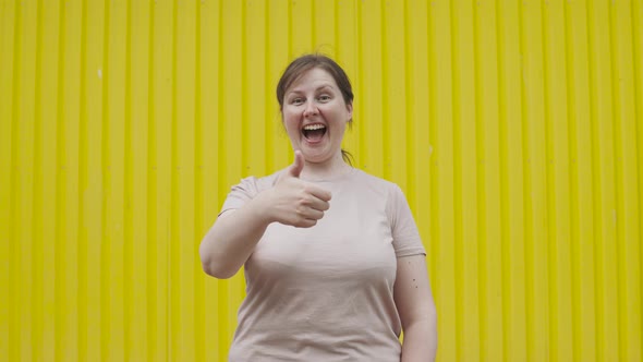 Positive Overweight Woman Showing Class Sign Thumbs Up Against Yellow Wall