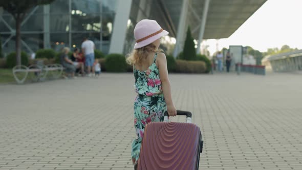 Child Girl Tourist with Suitcase Near Airport. Kid Wave Hand, Walks Down Street with Bag. Vacation