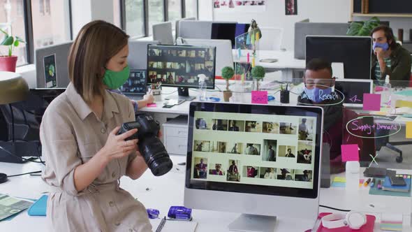 Caucasian businesswoman wearing face mask using a camera in modern office