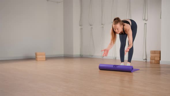 Woman rolling up yoga mat after training in studio. Girl folding fitness mat on floor at yoga studio