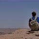 Young Man with Backpack Sitting on Cliff's Edge and Looking at the Desert - VideoHive Item for Sale