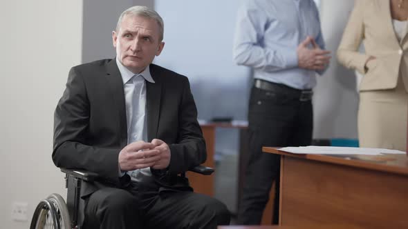 Frustrated Senior Caucasian Man Sitting in Wheelchair Looking Away with Blurred Unrecognizable